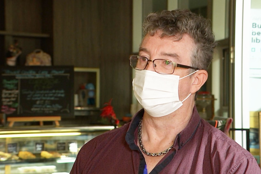 Ipswich cafe owner Gary Ladlay, wearing a face mask, speaks to the ABC