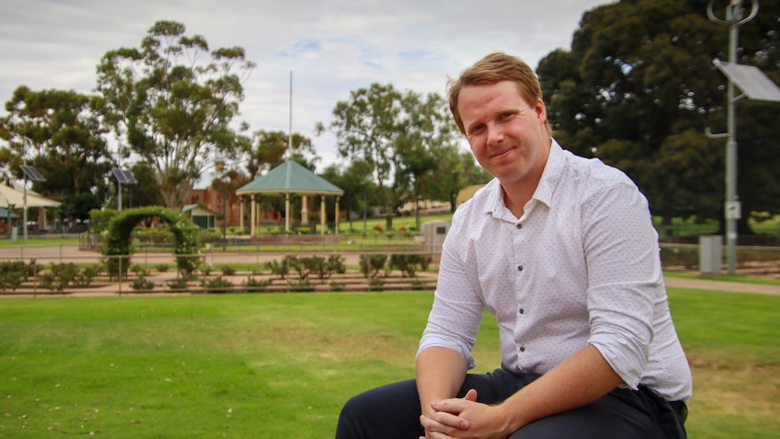 Patrick Reincke, sitting on a bench, with a local sports oval in the background.