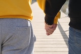 Two people, who cannot be identified, hold hands as they walk down an outdoor walkway.