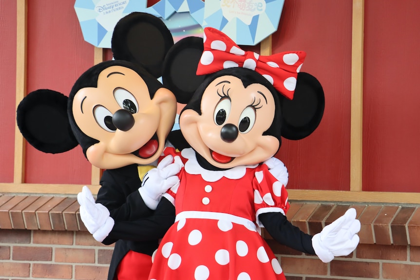 People wearing Mickey and Minnie Mouse costumes pose for a photo near a brick ledge.