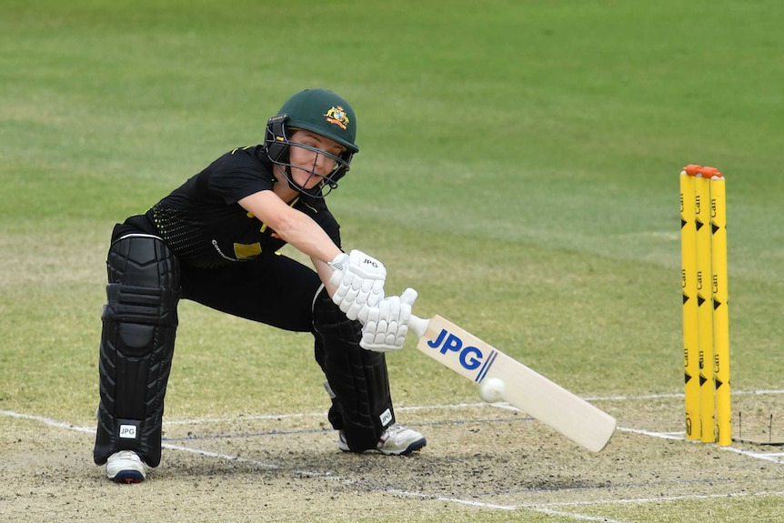 An Australian female cricketer batting stretches to her left to play a wide delivery against New Zealand.