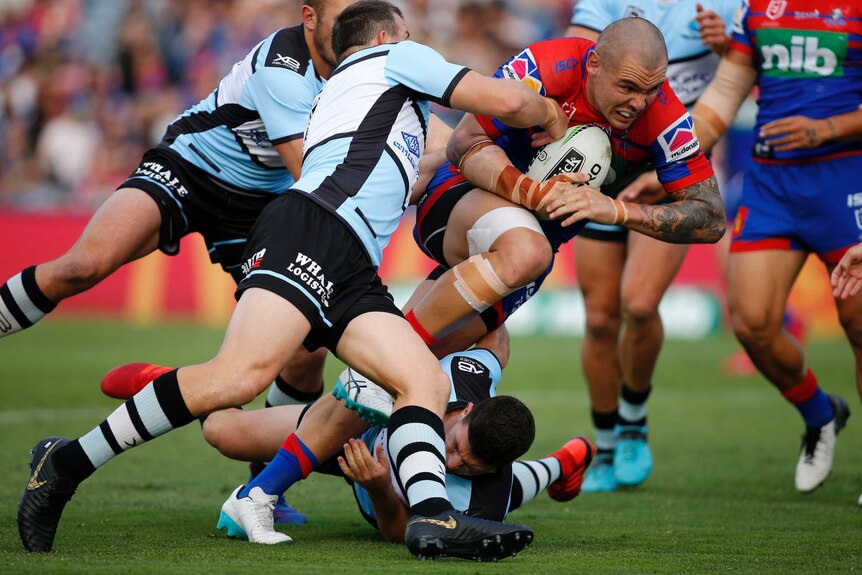 David Klemmer runs the balls, as three Sharks players attempt to tackle him.