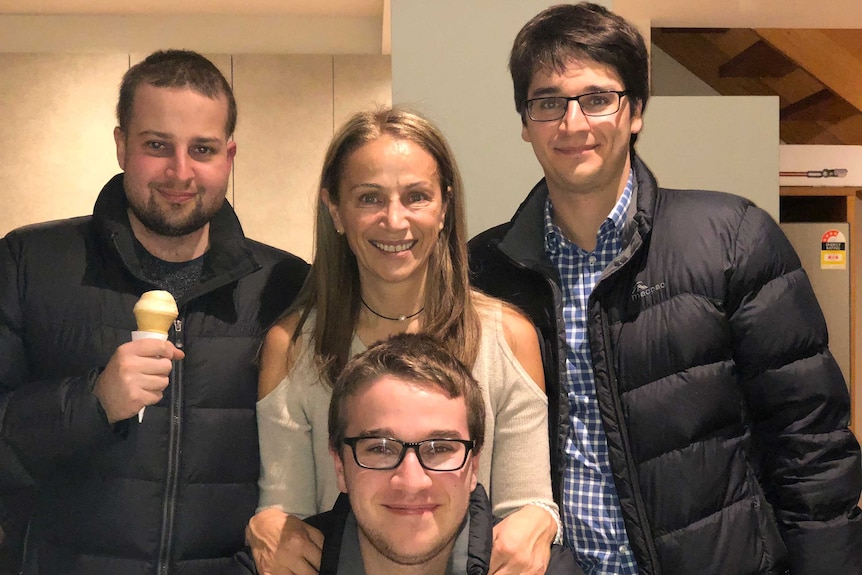 Samuel holding an ice cream as he stands in a kitchen with his mother Elly and brothers Raphael and Joel.