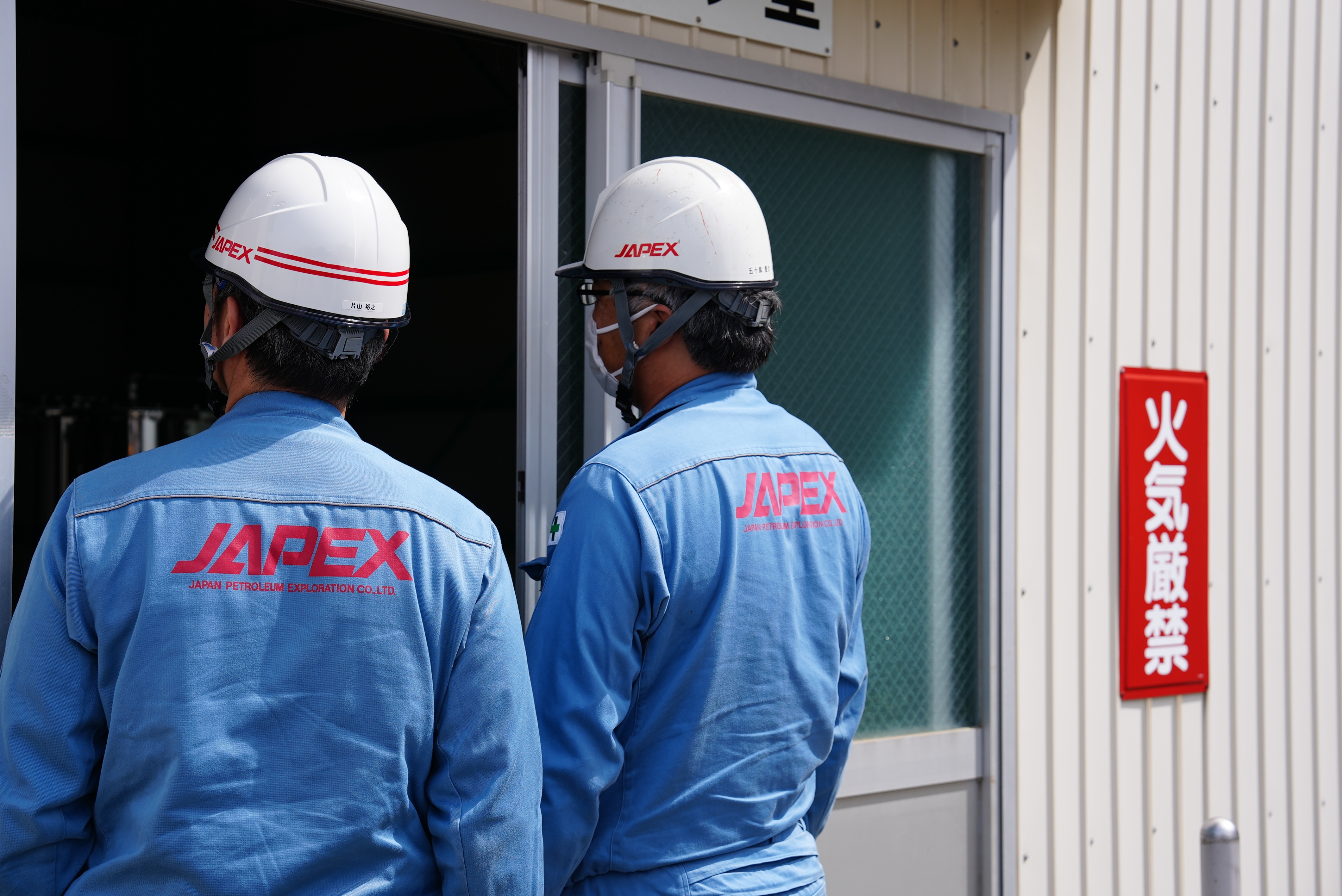Two workers wearing hard hats observe a room.