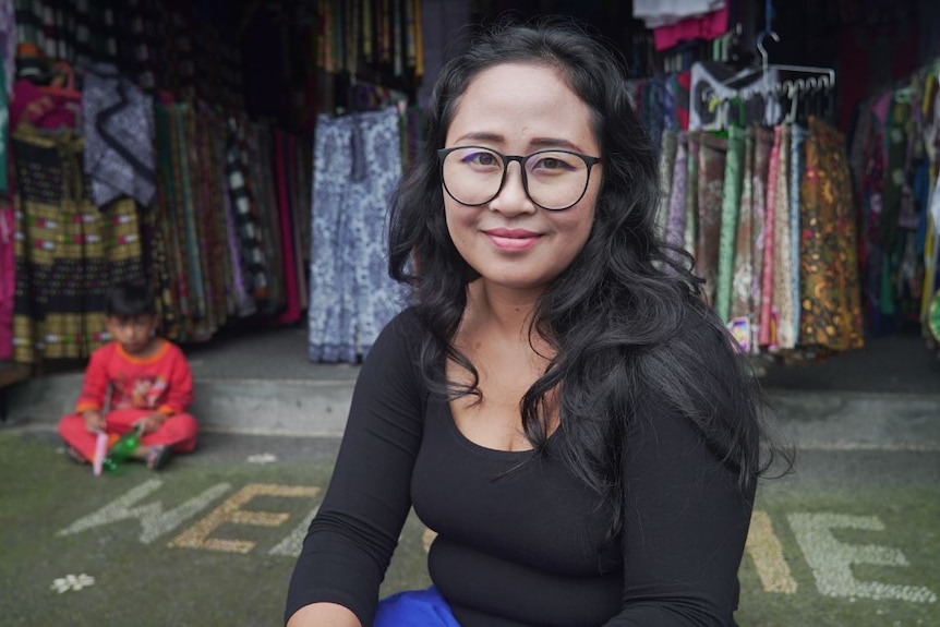 I Gusti Ayu Nia Arsiani smiles at the camera while sitting in front of her clothes shop.