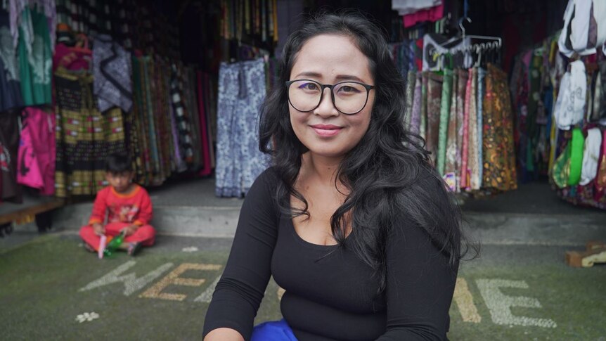 I Gusti Ayu Nia Arsiani smiles at the camera while sitting in front of her clothes shop.