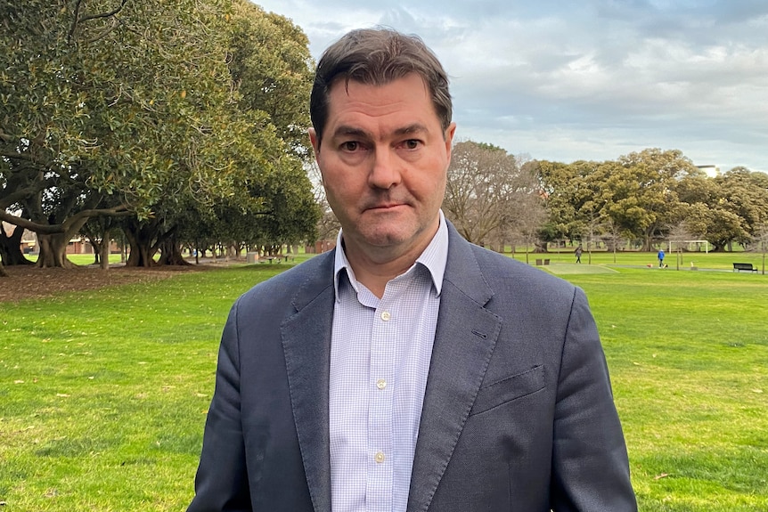 A man in a suit jacket looks at the camera.