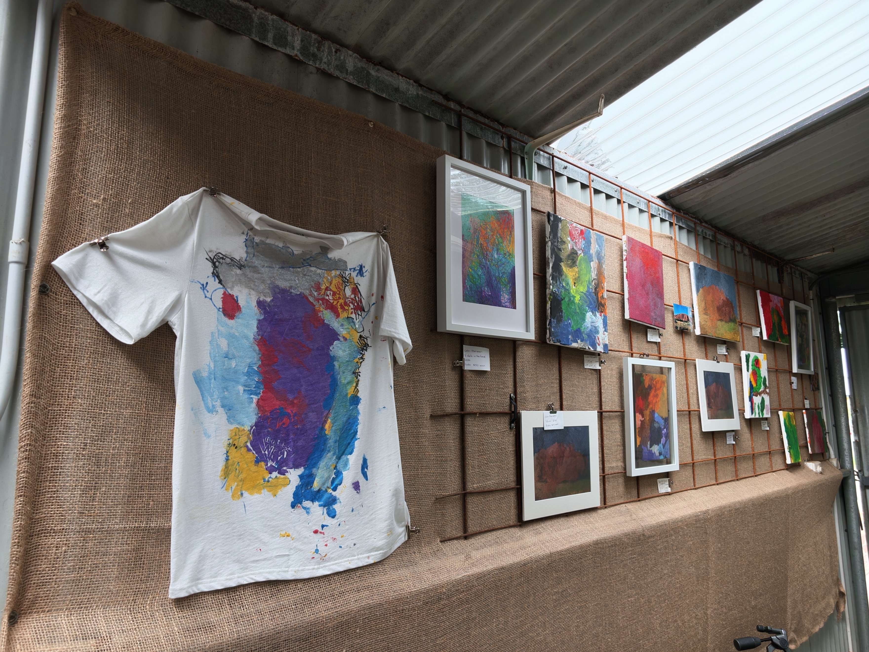 A hessian backdrop on a wall featuring a brightly painted T-shirt and artworks.