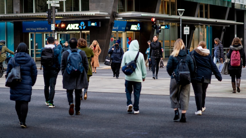 People wearing winter clothes cross diagonally at a pedestrian crossing with an ANZ bank branch in the background