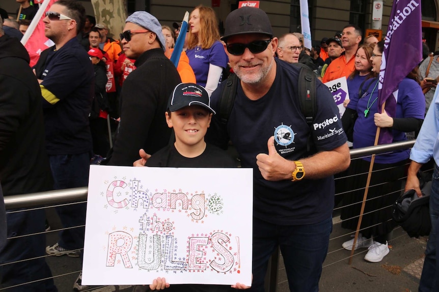A young boy holding a sign reading 'change the rules' with his dad.