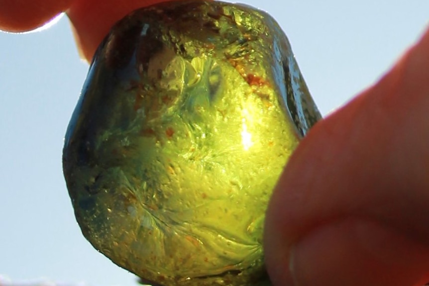 The sun shines through a large green gem stone held between two fingers.