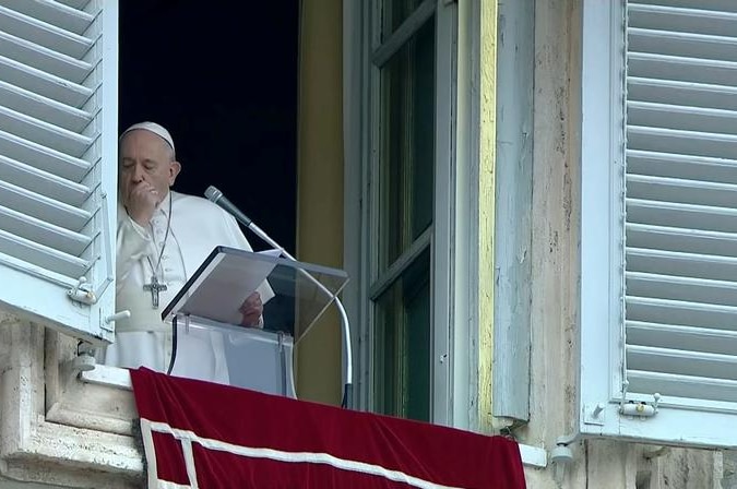 Pope Francis standing by the window coughing.