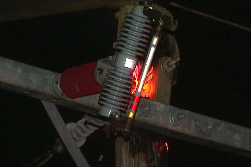 A close-up shot of a burning power pole top with an electricity transmitter around it.