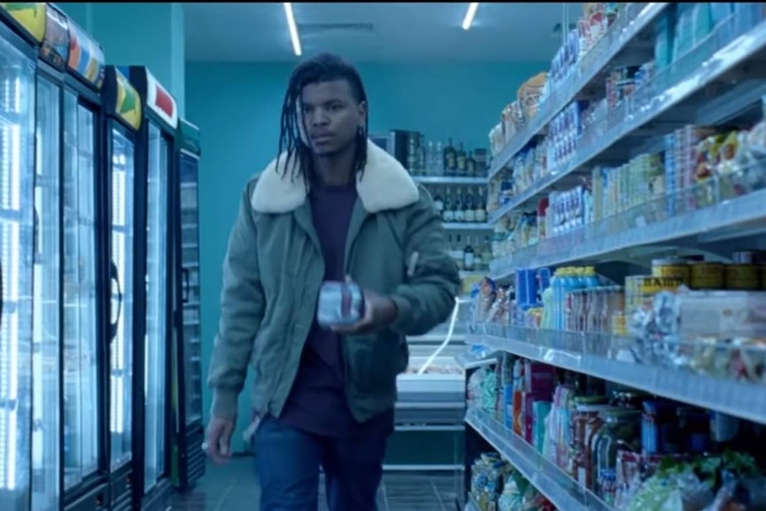 A young man walks down a supermarket aisle carrying a packet of period pads.