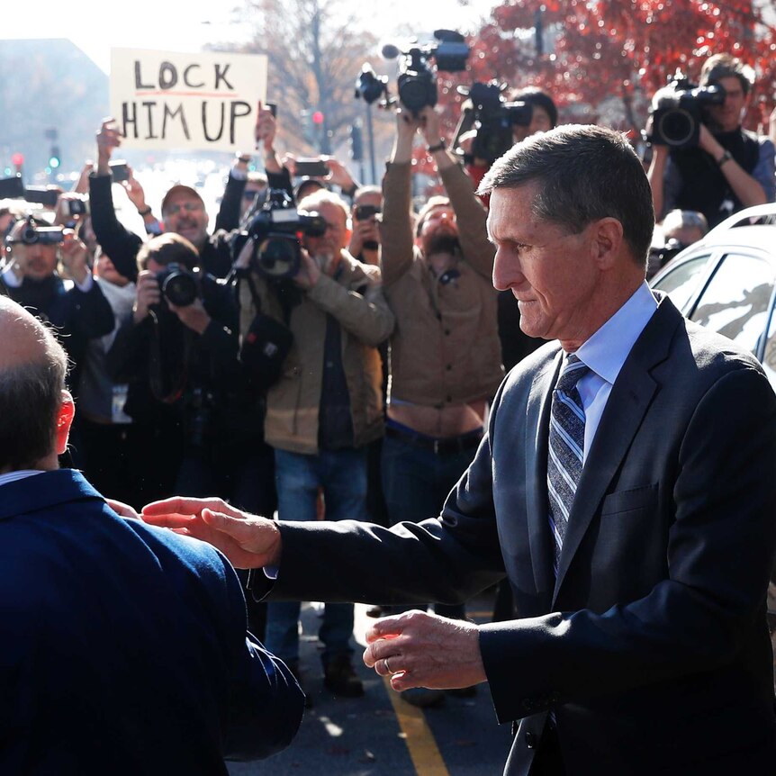 Michael Flynn is photographed by paparazzi and confronted by a protester with a sign reading "Lock him up"