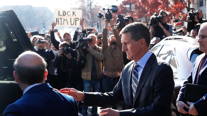 Michael Flynn is photographed by paparazzi and confronted by a protester with a sign reading "Lock him up"