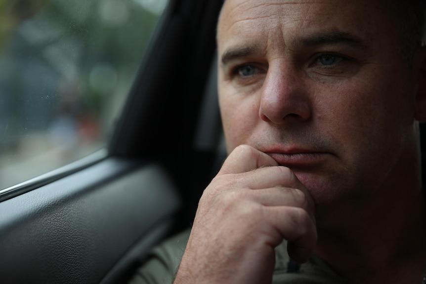 Close up of man looking out a car window while resting his hand on his chin.