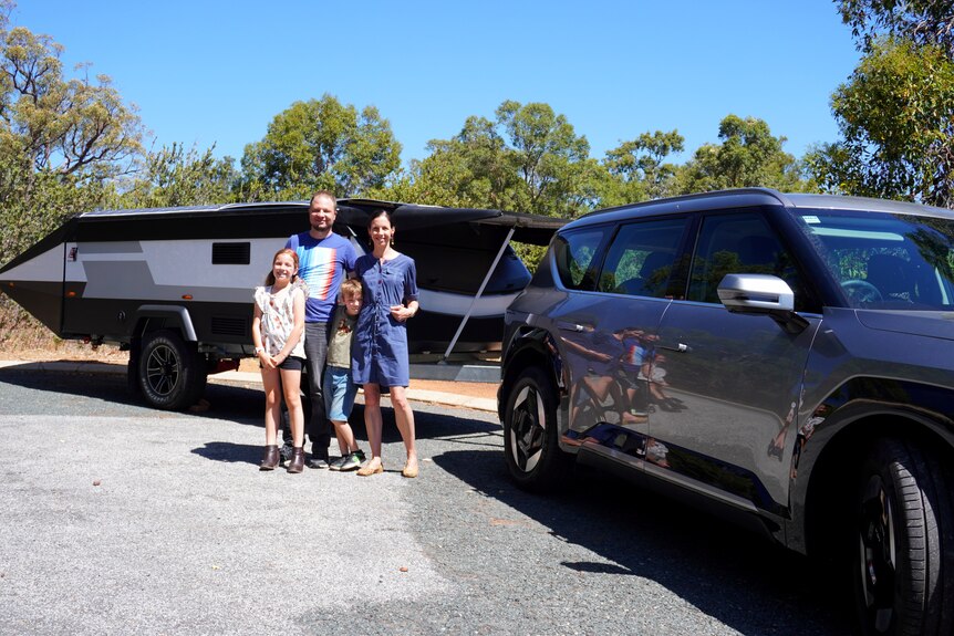 A family standing next to a four-wheel drive and caravan.