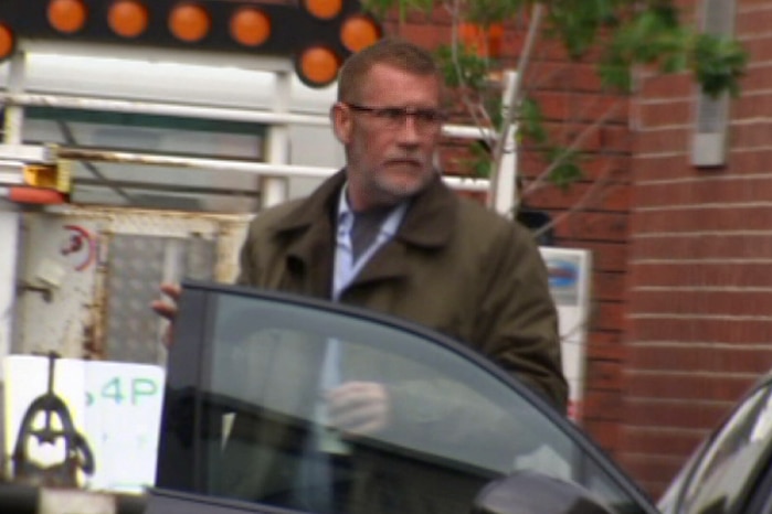 Phillip Whiteman, wearing a brown jacket and glasses, exits a car.