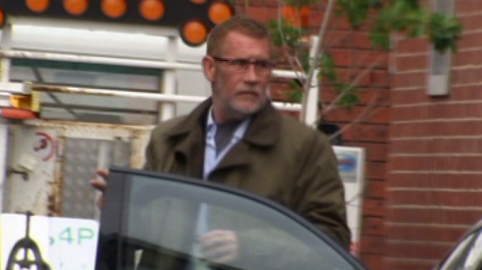 Phillip Whiteman, wearing a brown jacket and glasses, exits a car.