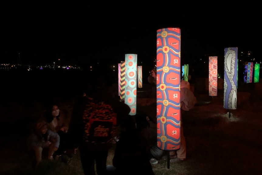 A group of lit up cylinders with colourful patterns at night at the Vivid festival.
