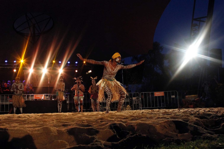 An Aboriginal man dancers in a grass skirt with marking in white paint on his body.