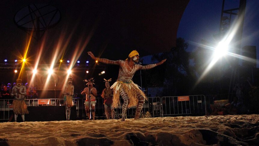 An Aboriginal man dancers in a grass skirt with marking in white paint on his body.
