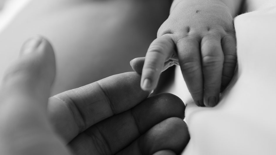 A parent's hand touches their baby's little fingers.