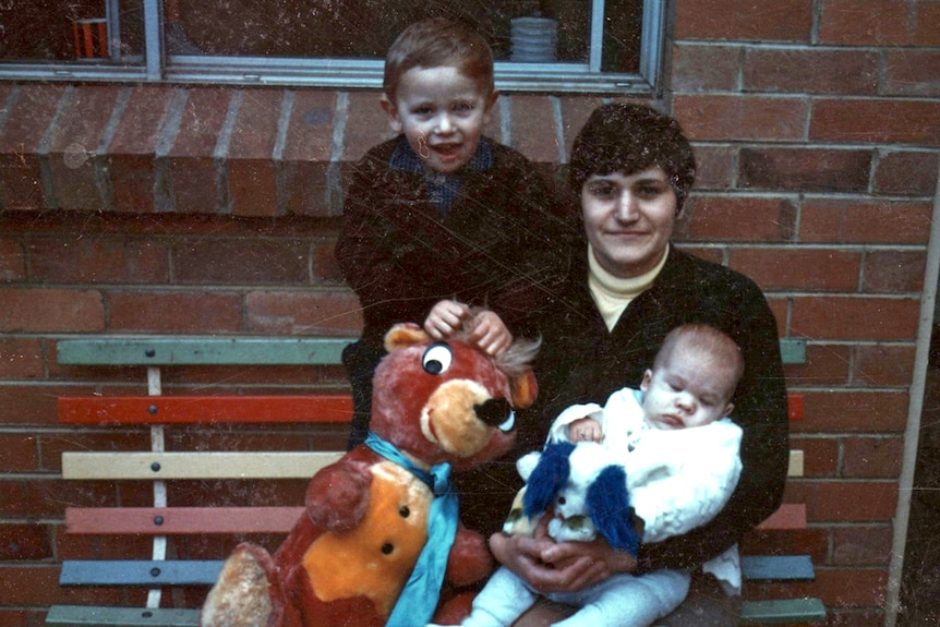 Maria James sits holding her youngest son Adam, beside her sits her oldest son Mark and a large stuffed animal.