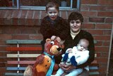 Maria James sits holding her youngest son Adam, beside her sits her oldest son Mark and a large stuffed animal.