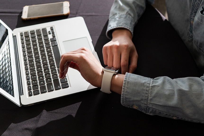 An unidentified person checks the time on her watch while working on a laptop.