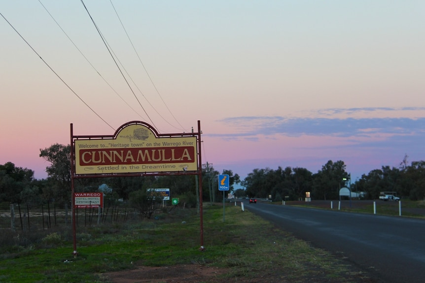 A town sign alongside a road with a dusty pink sky in the background.