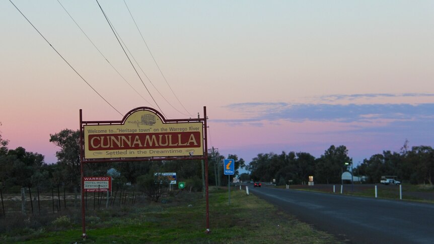 A town sign alongside a road with a dusty pink sky in the background.