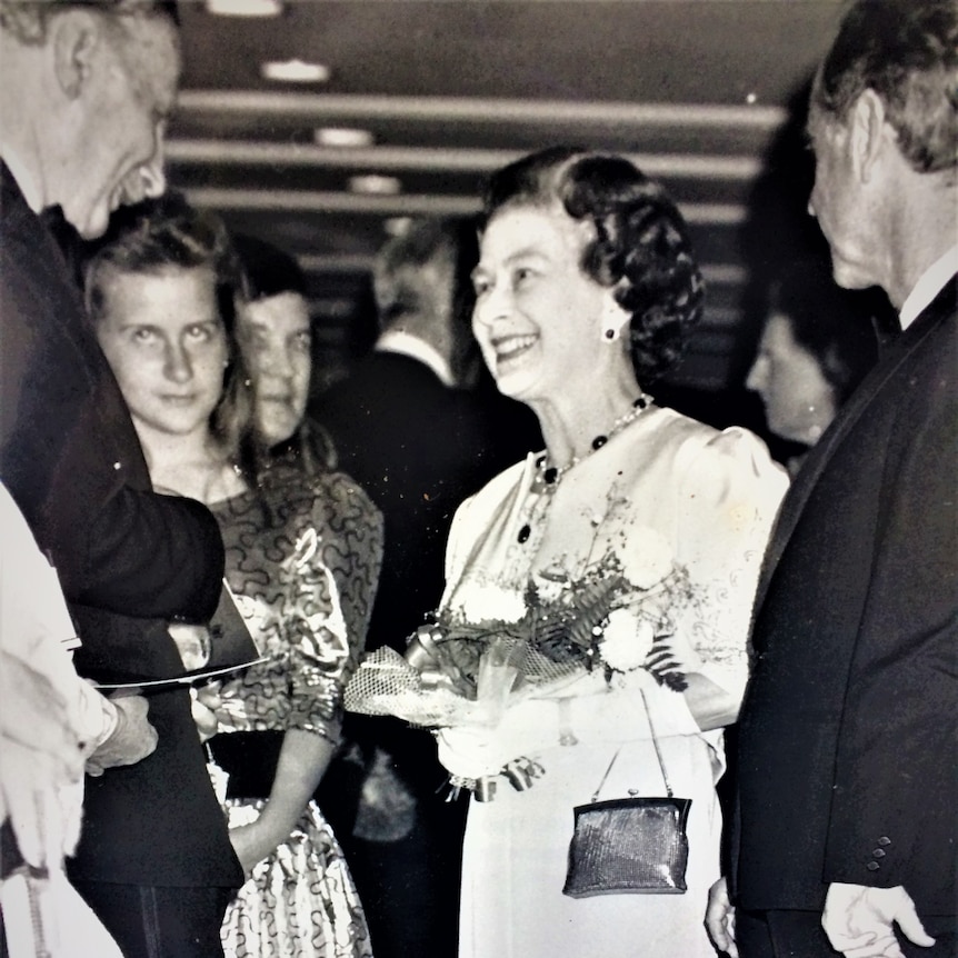 A black-and-white photograph of the Queen amongst a crowd.