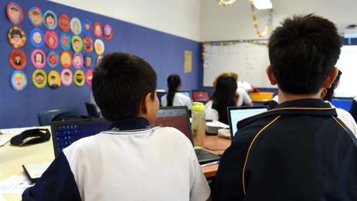 Two students have their backs to the camera as they sit at a classroom desk.