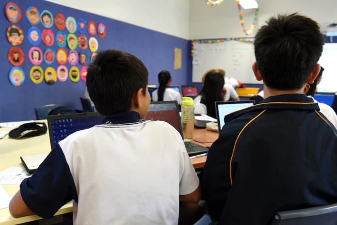 Two students have their backs to the camera as they sit at a classroom desk.