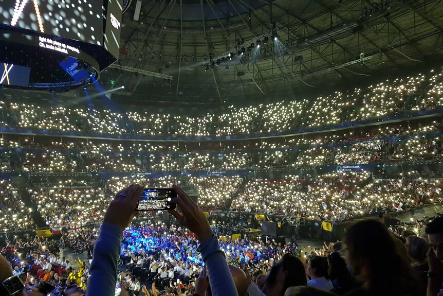 A person holds up their phone in a stadium full of lights.