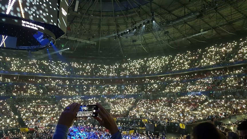 A person holds up their phone in a stadium full of lights.