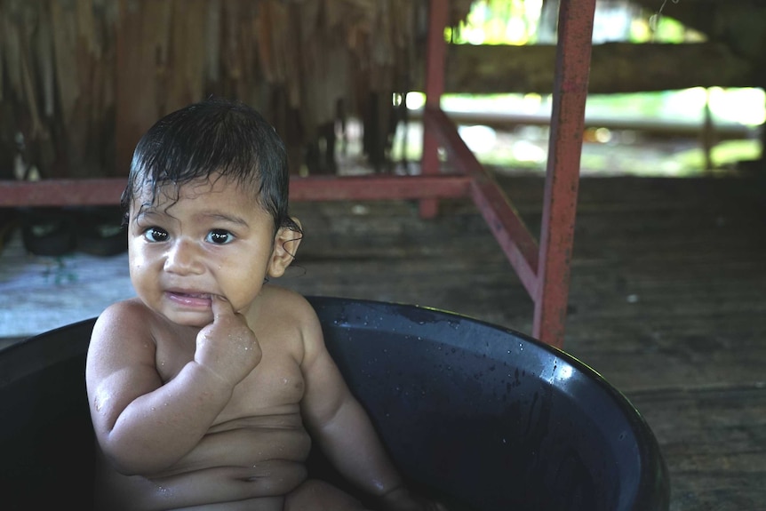 A baby sits in a bucket filled with water