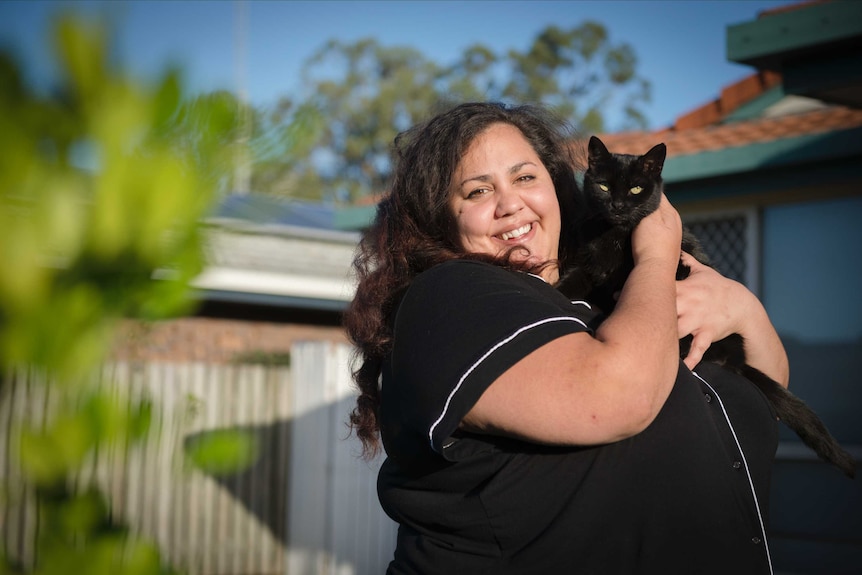 The comedian Steph Tisdell standing in a backyard with a cat