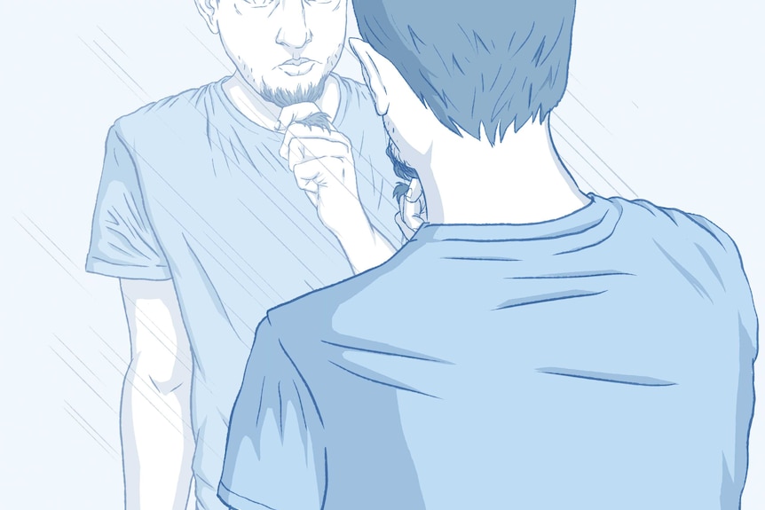 A man stares into his reflection, pulling at a section of his beard, wearing a t-shirt.