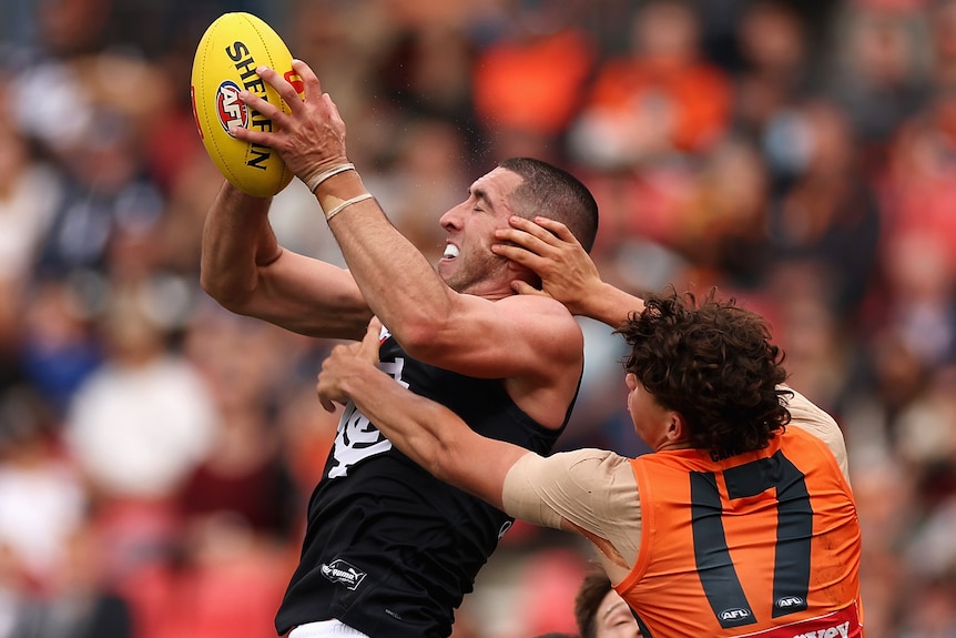 A Carlton AFL player marks the ball with both hands as he is challenged in the air by a GWS opponent.