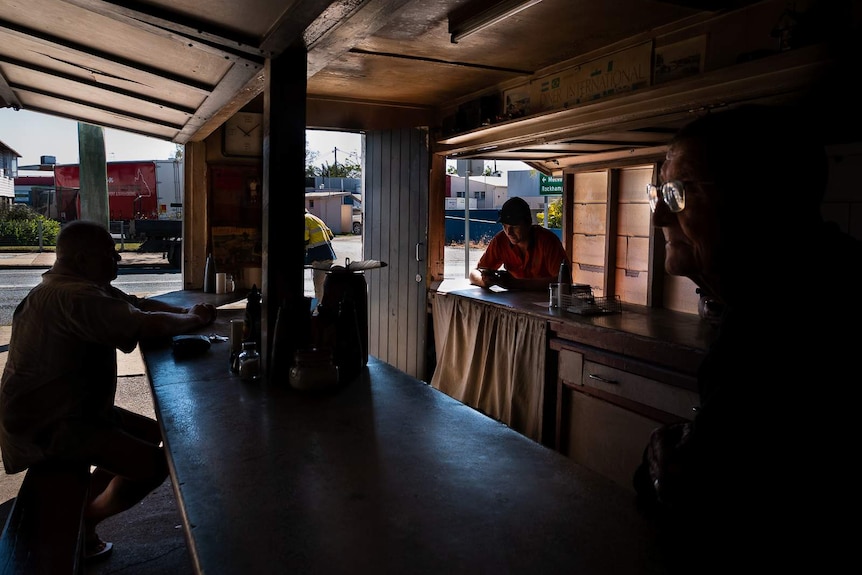 The inside of the pie cart, with wooden panelling and old wooden counter tops, two customers are dining in, Rosco in foreground.