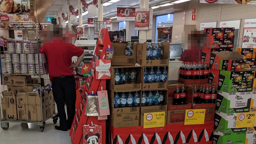 A Coles employee with a rack of a2 baby formula near the checkout.