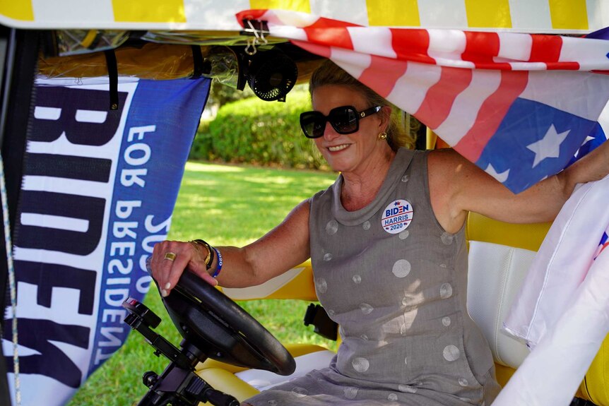 A woman sits on a golf cart wearing a Biden Harris 2020 badge