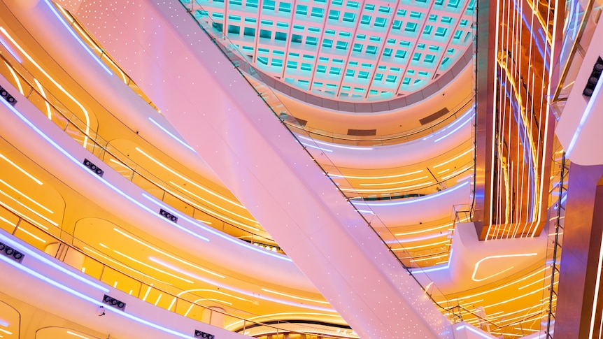 You look up at a bright mall atrium, bathed in pink and yellow mood lighting. 