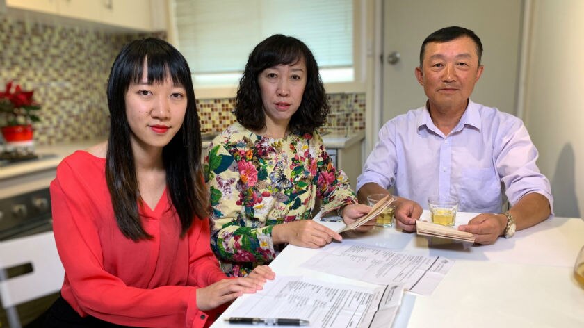 Three people sitting at a kitchen table with paperwork.