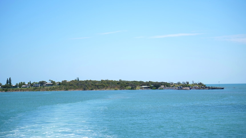An island in the distance with blue water in the foreground of the photo