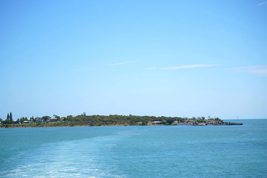 An island in the distance with blue water in the foreground of the photo.