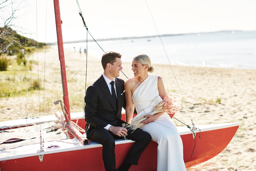 Chloe and James Devery on their wedding day, sitting on a beached yacht.